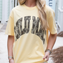 Person wearing a yellow t-shirt with text, standing outdoors.
