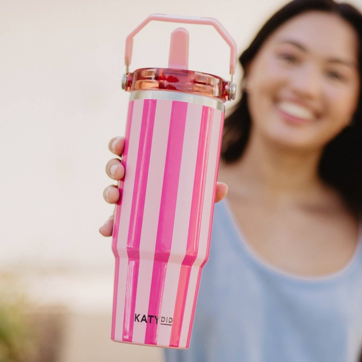 Person holding a pink striped water bottle with 'KATYDID' branding.