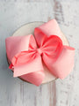 Large pink bow on a circular white object with a light wooden background