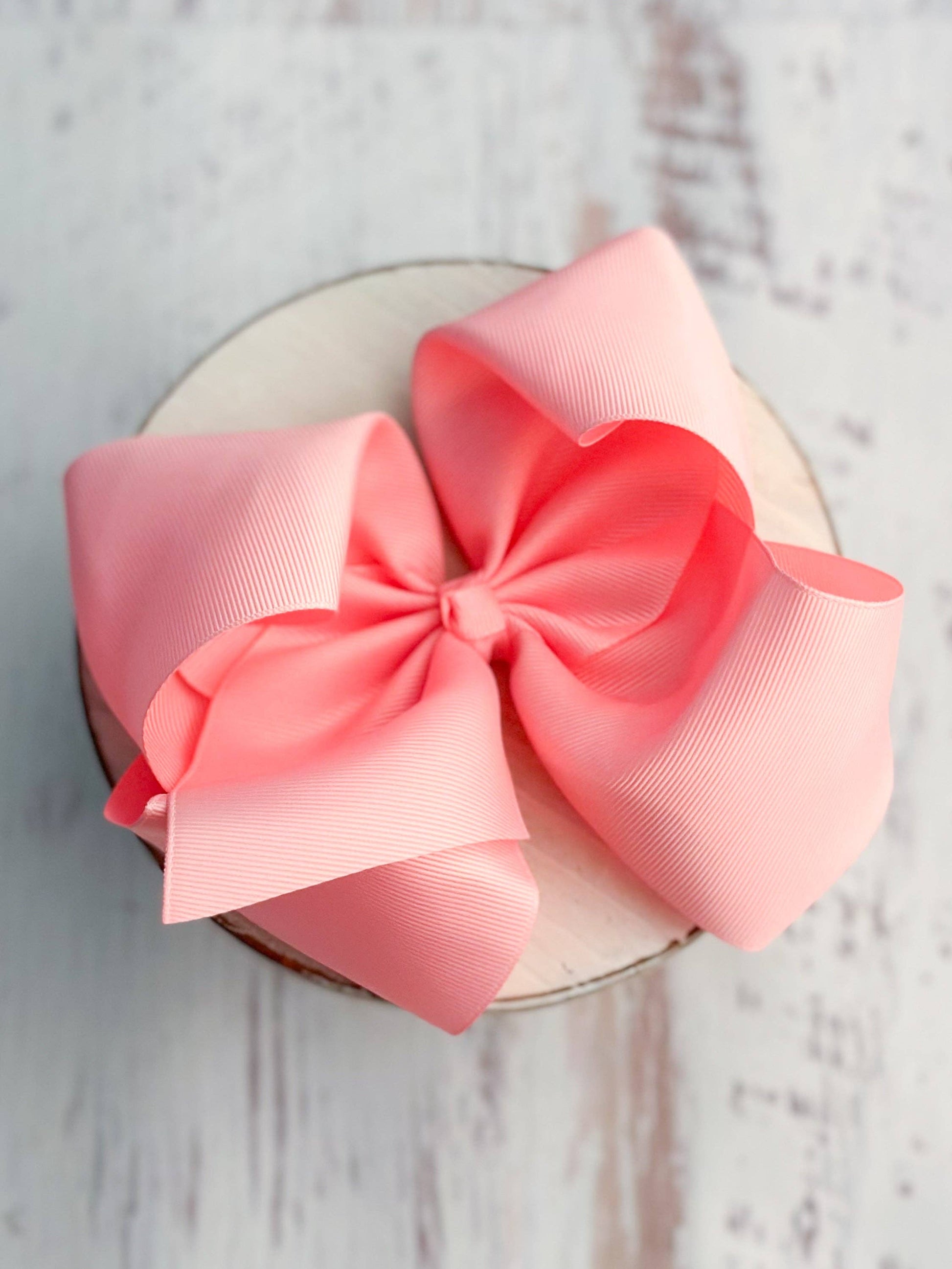Large pink bow on a circular white object with a light wooden background