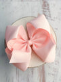 Large pink bow on a white circular base against a light wooden background