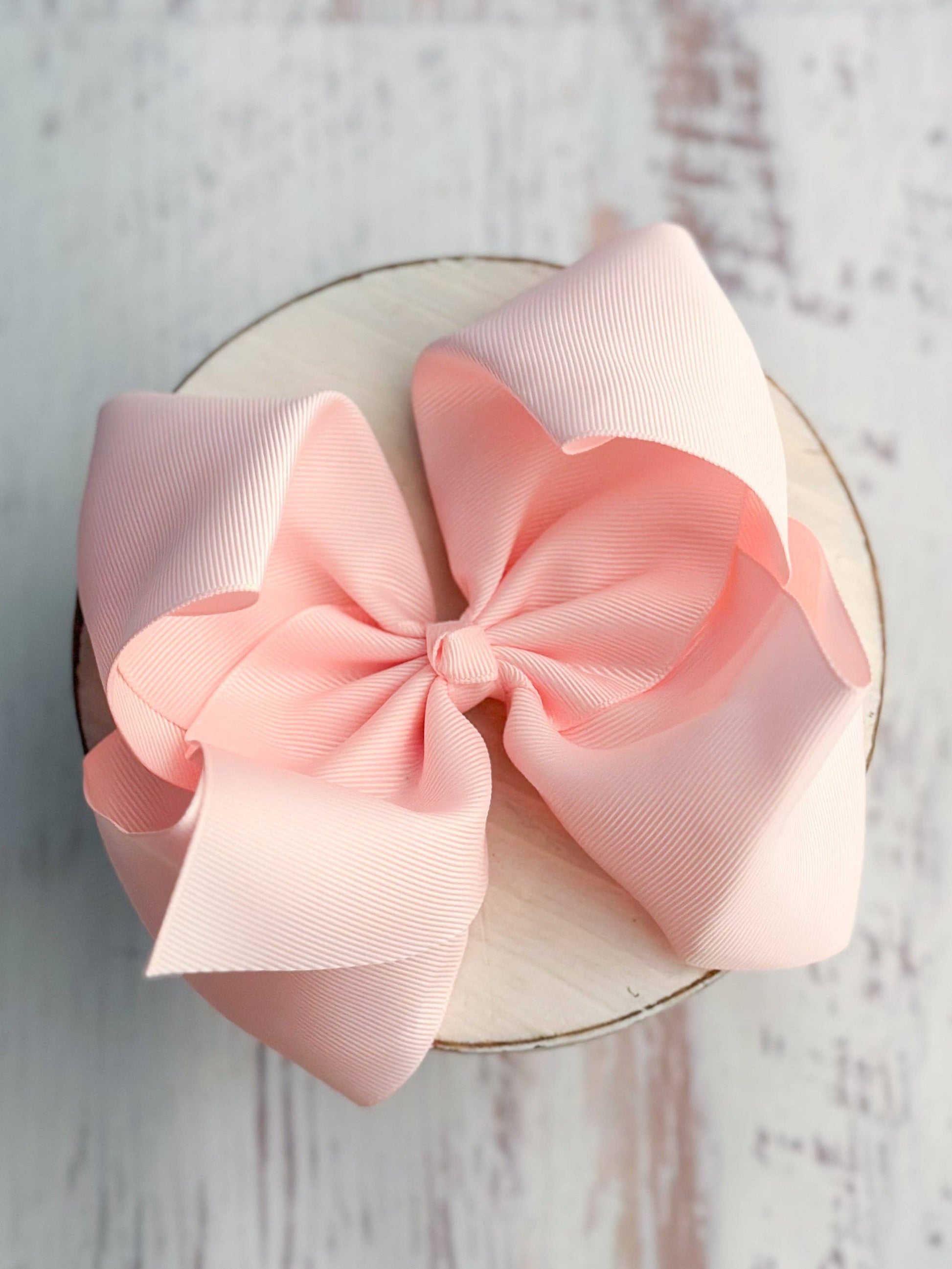 Large pink bow on a white circular base against a light wooden background