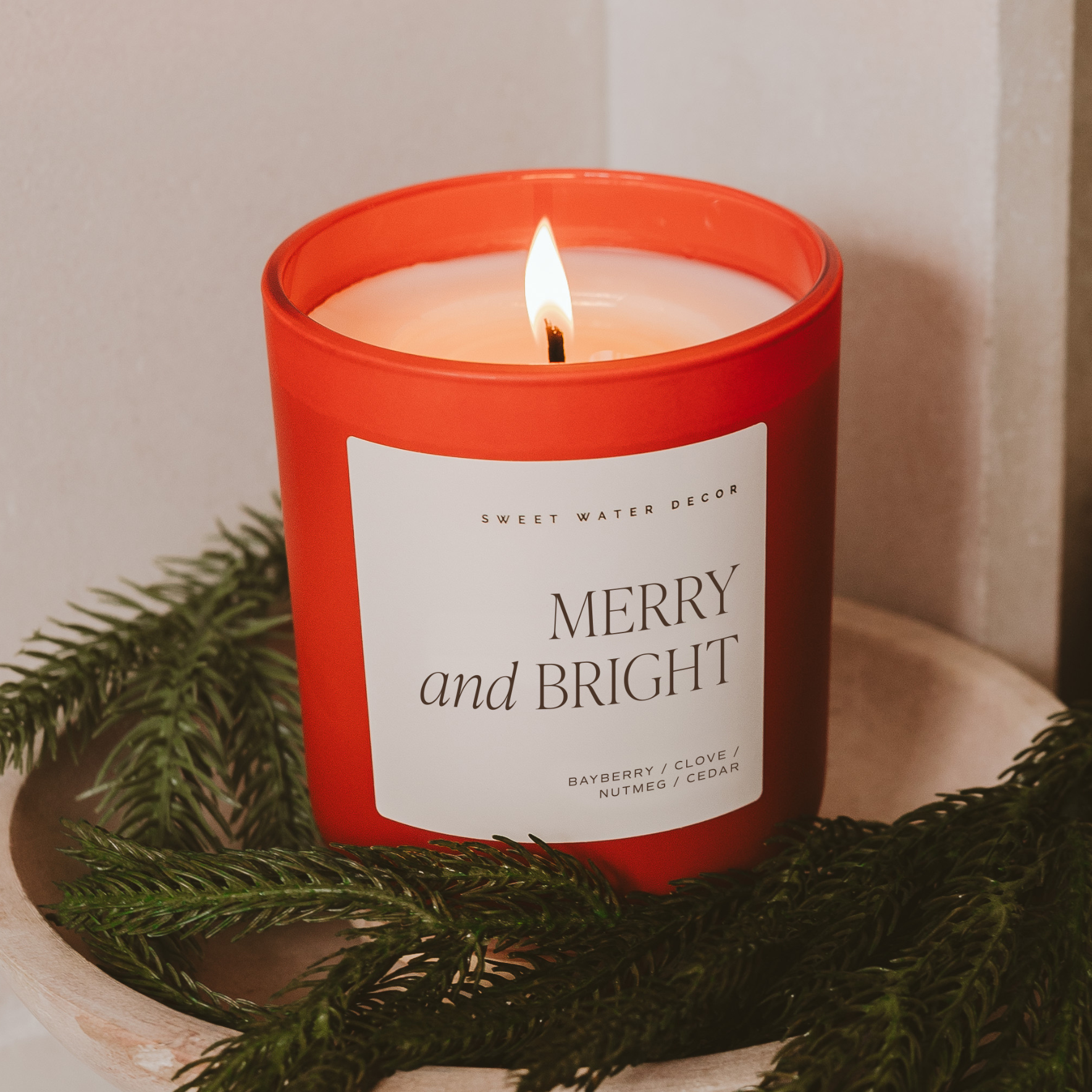 Candle with 'Merry and Bright' label surrounded by greenery