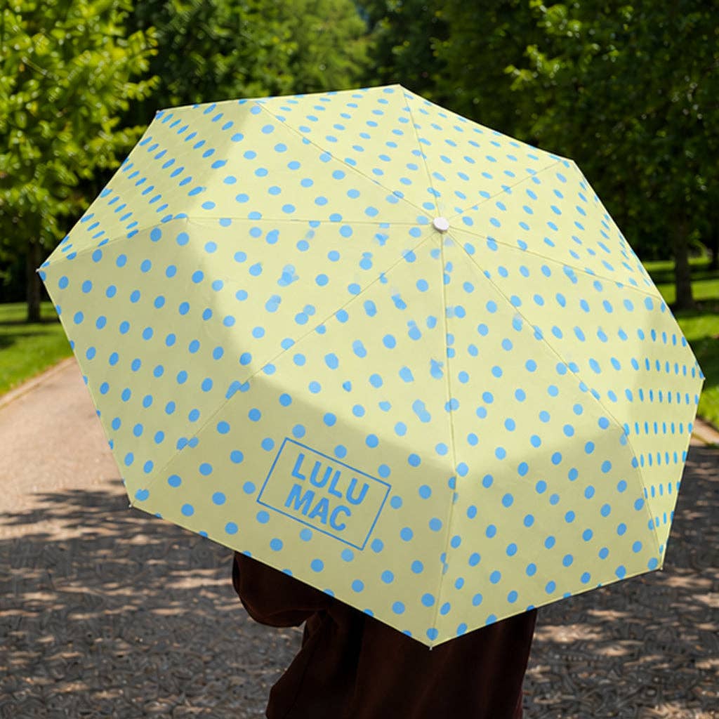 Yellow umbrella with blue polka dots held by a person outdoors