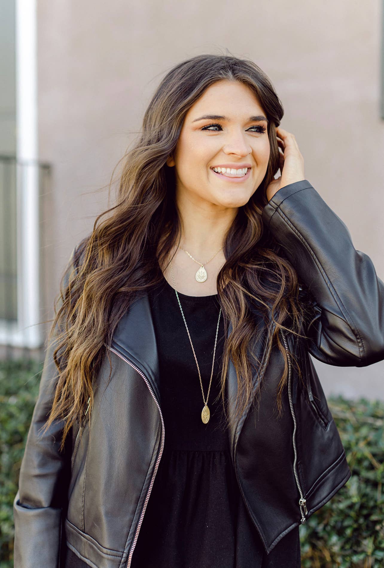 Woman wearing a black leather jacket and black dress, standing outdoors.