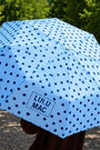 Blue polka dot umbrella with 'LULU MAC' branding held outdoors.