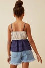 Back view of a person wearing a layered top and denim shorts on a beige background