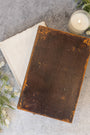 Vintage leather-bound book on a textured surface with a candle and greenery
