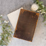 Vintage leather-bound book on a textured surface with a candle and greenery