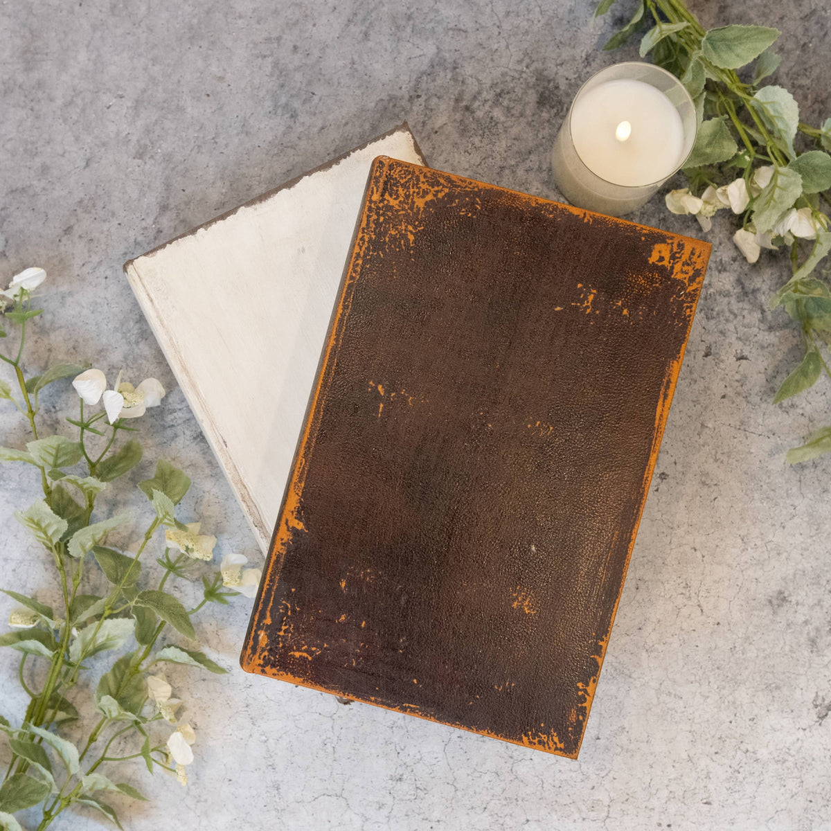 Vintage leather-bound book on a textured surface with a candle and greenery