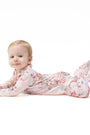 A baby lying on their stomach wearing a light pink footed sleeper with a delicate floral pattern, photographed against a seamless white background.