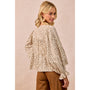 A woman wearing a beige and brown leopard-print blouse with long ruffled sleeves, shown from the back against a solid beige background.