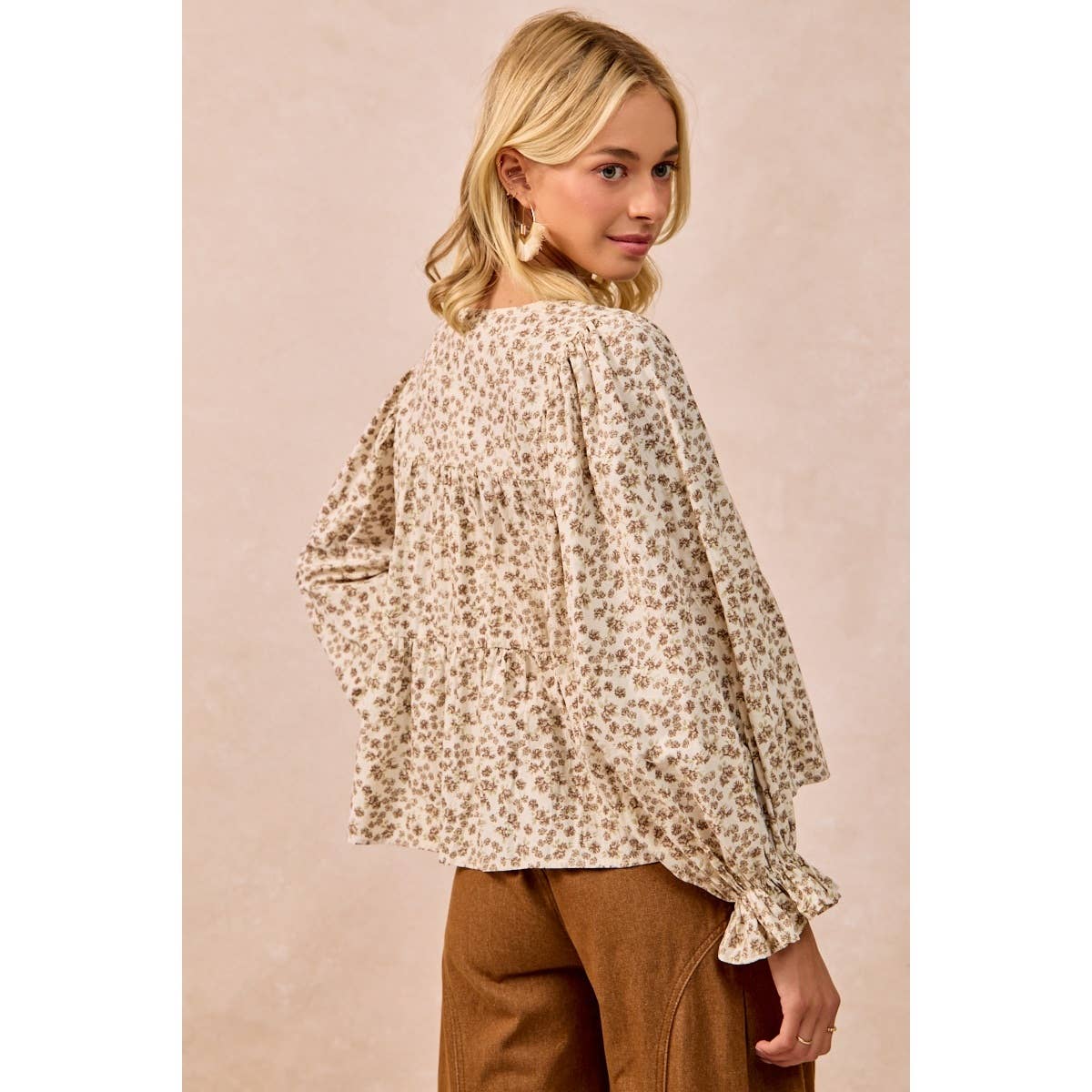 A woman wearing a beige and brown leopard-print blouse with long ruffled sleeves, shown from the back against a solid beige background.