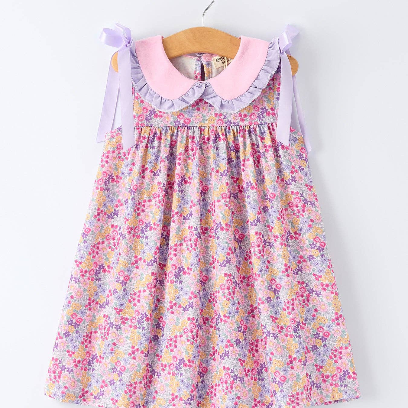 Floral dress with a pink collar on a hanger against a white background