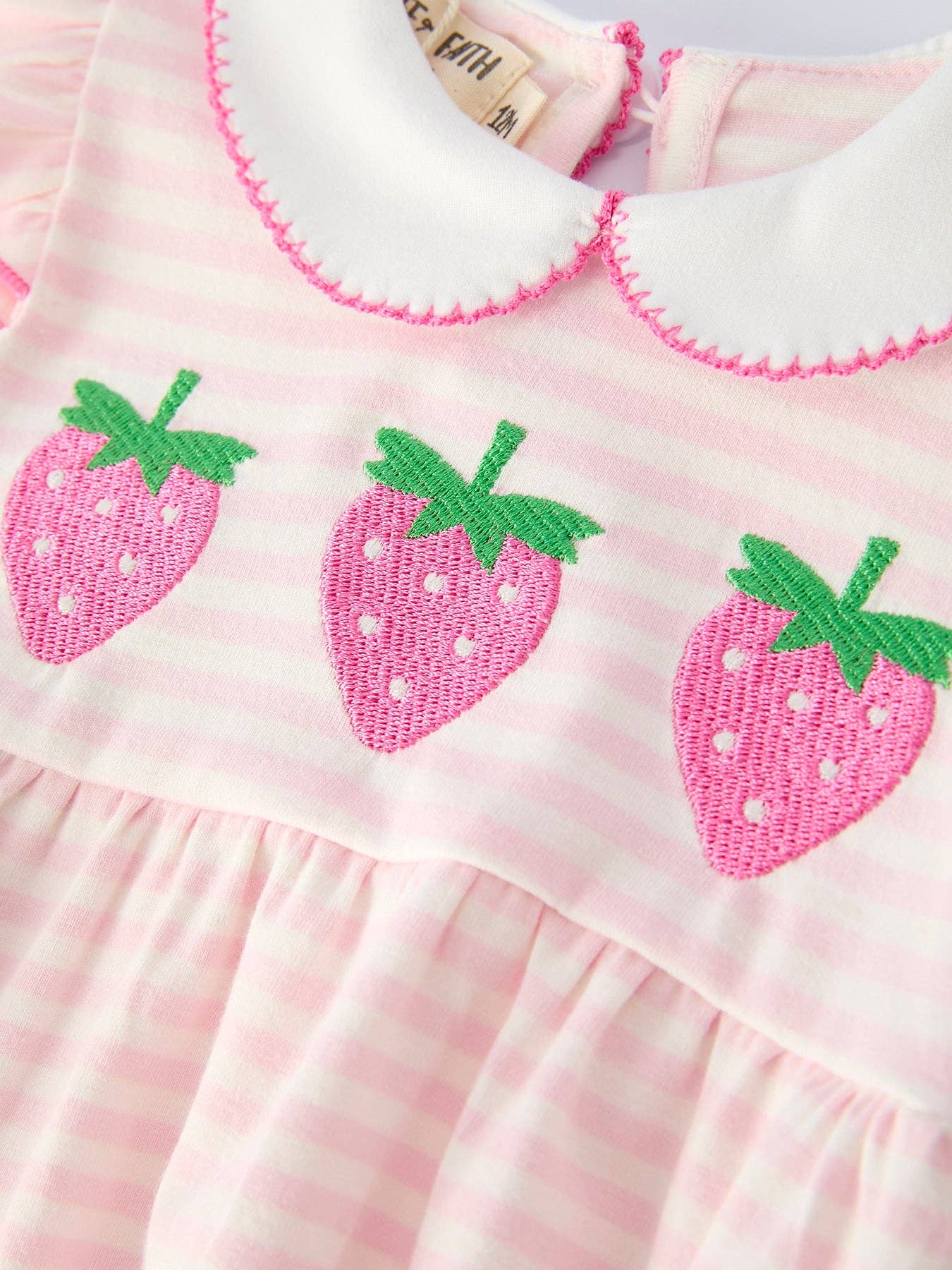 Pink dress with strawberry patterns and a brand label on a white background