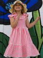 Young girl in a pink and white striped dress and sun hat standing in front of a colorful mural.