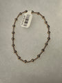 A beaded bracelet made of small metallic dark bronze beads, shown on a textured light gray background with a white product tag attached.