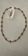 A beaded bracelet made of small metallic dark bronze beads, shown on a textured light gray background with a white product tag attached.