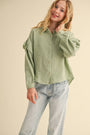Girl wearing a green textured shirt and light blue jeans on a beige background