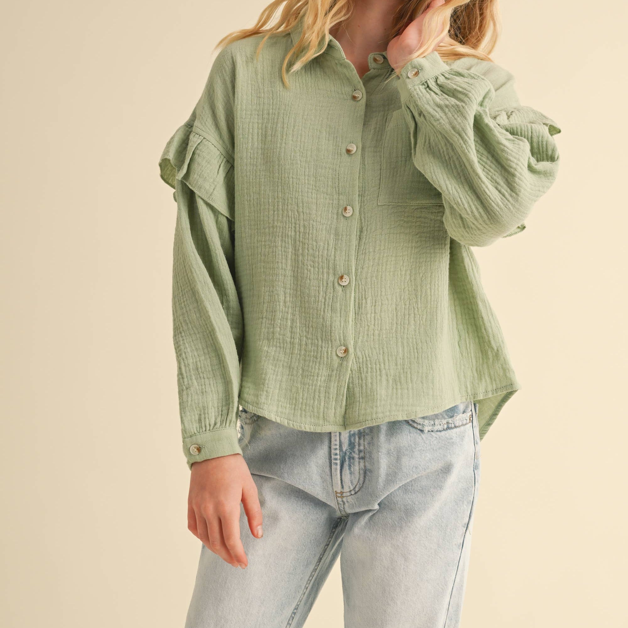Girl wearing a green textured shirt and light blue jeans on a beige background