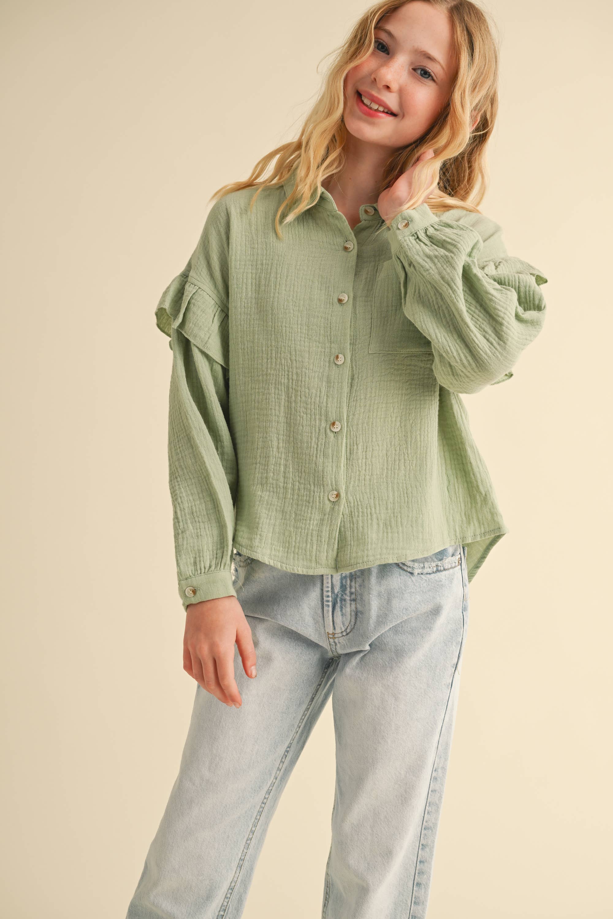 Girl wearing a green textured shirt and light blue jeans on a beige background