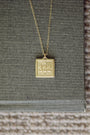 Gold necklace with a square pendant displaying the number '322' on a textured surface.