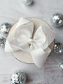 White decorative bow on a round white box with silver ornaments in the background