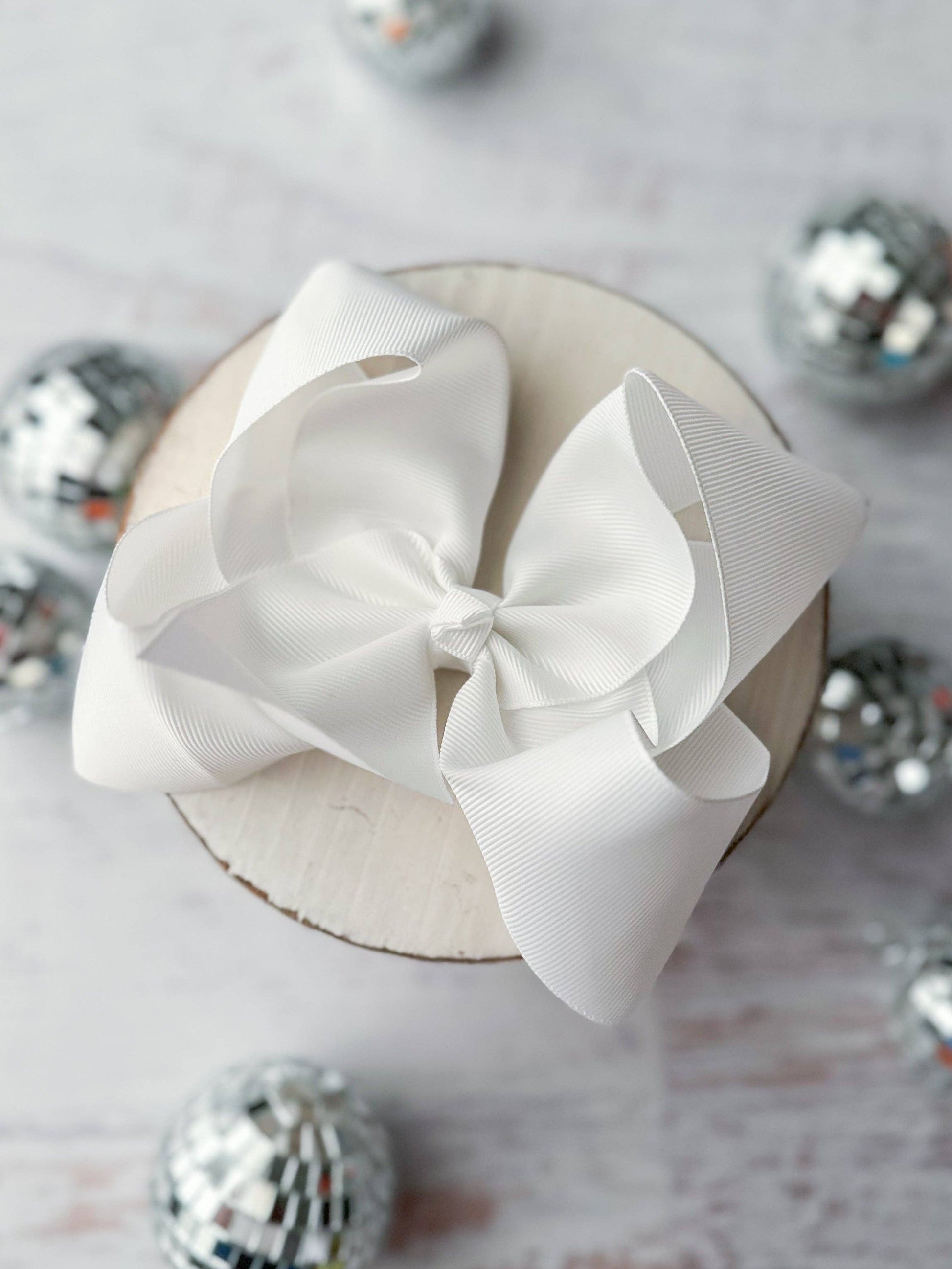 White decorative bow on a round white box with silver ornaments in the background