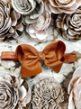 Brown bow headband on a textured surface with floral decorations