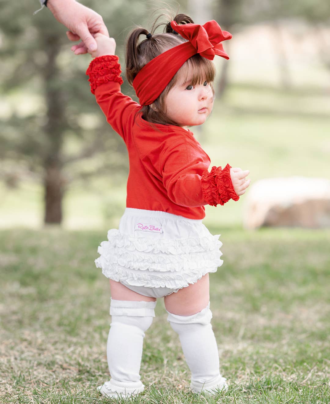 Child wearing a red top, white ruffled skirt, and white knee-high socks outdoors.