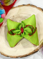 Green hair bow with red accents on a wooden surface