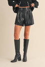 Person wearing black leather shorts and knee-high boots on a beige background