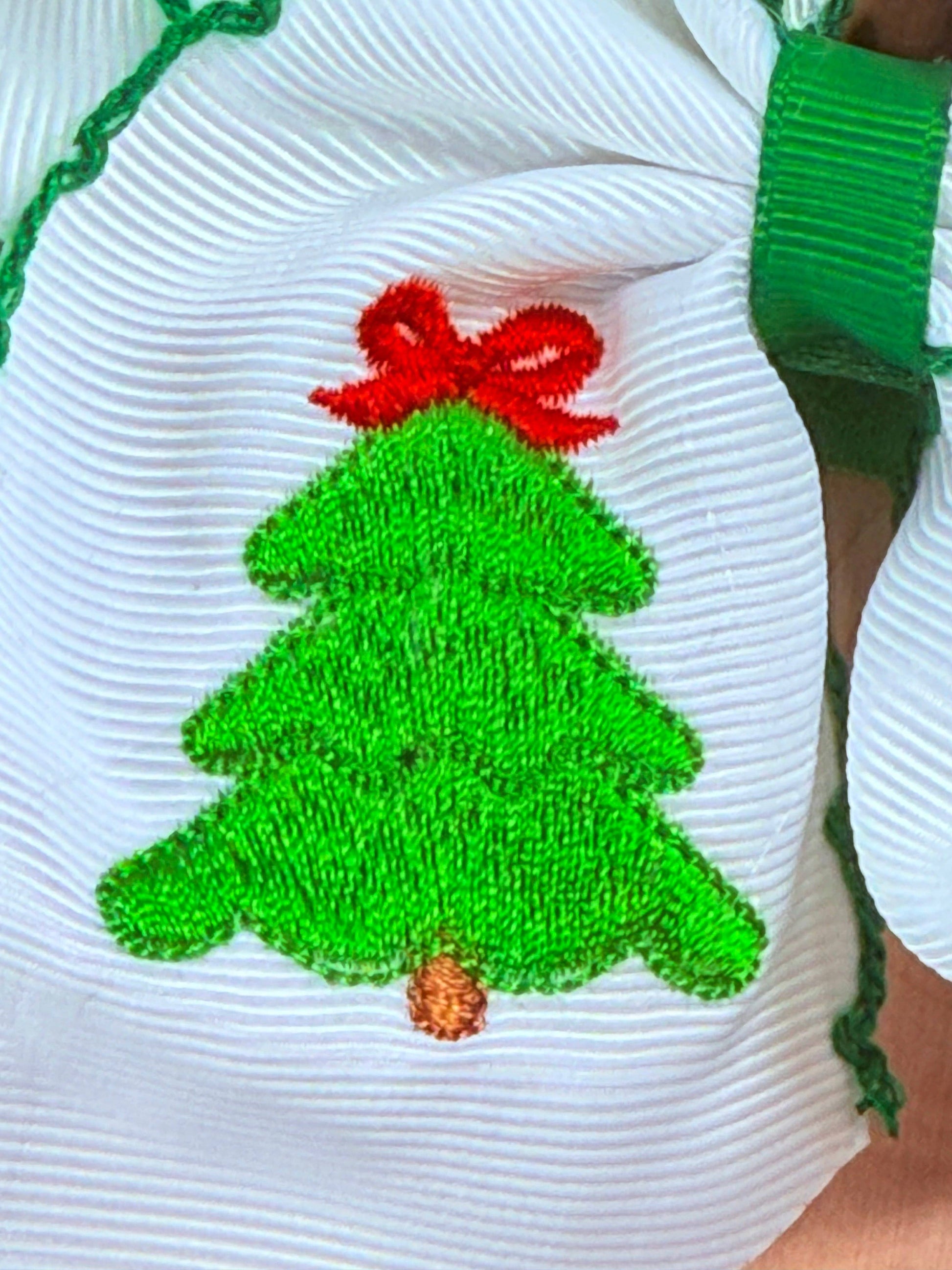 Green embroidered Christmas tree design on a white fabric background with a red bow.