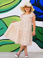 Young girl in a floral dress and sun hat standing in front of a colorful mural.