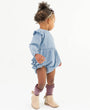 Child wearing a blue denim romper with ruffles on a white background