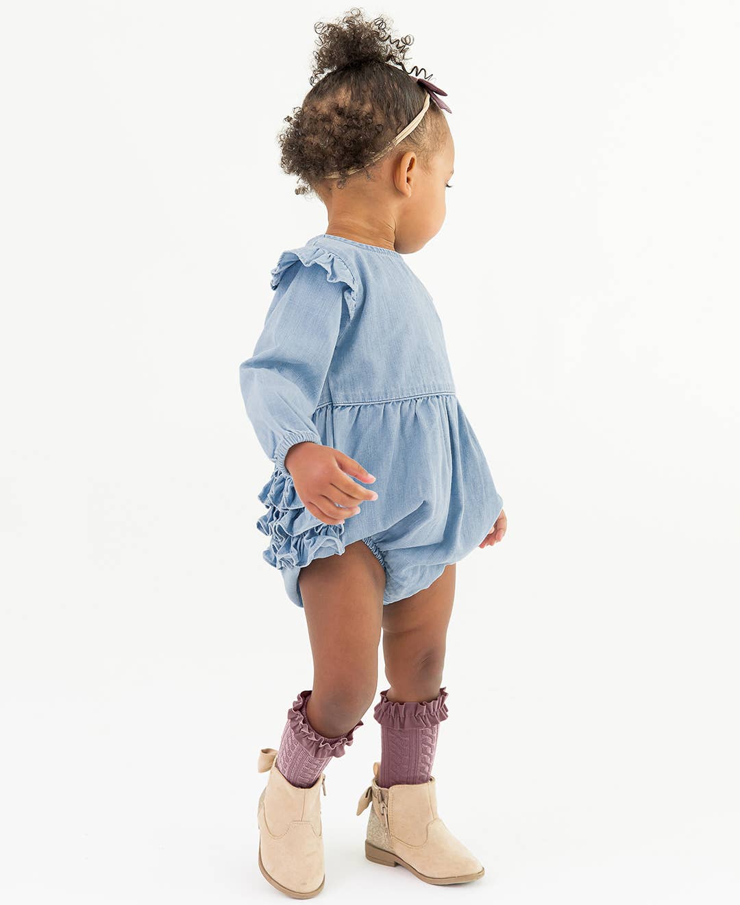 Child wearing a blue denim romper with ruffles on a white background