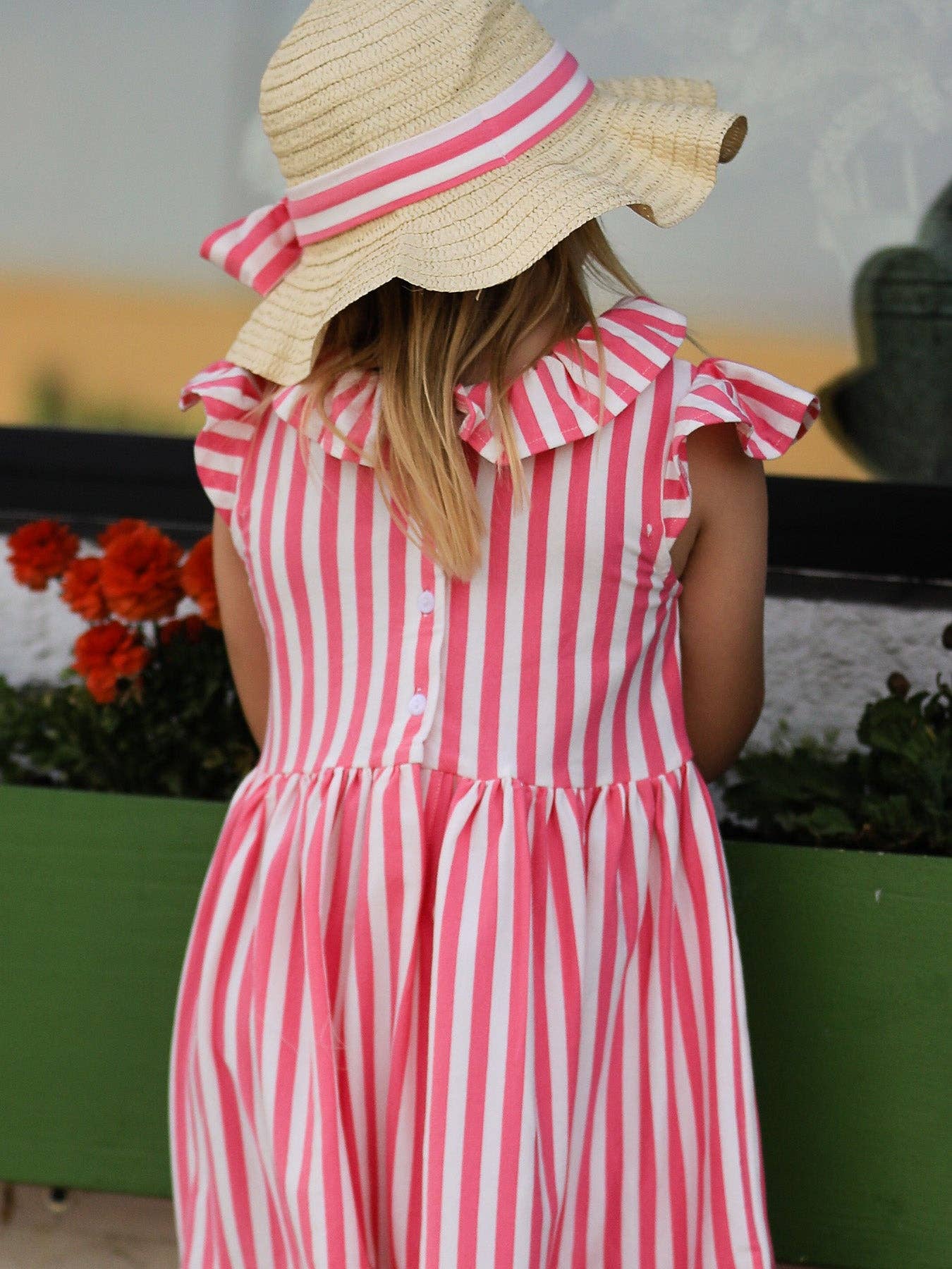 Person wearing a pink and white striped dress with a wide-brimmed hat in an outdoor setting.