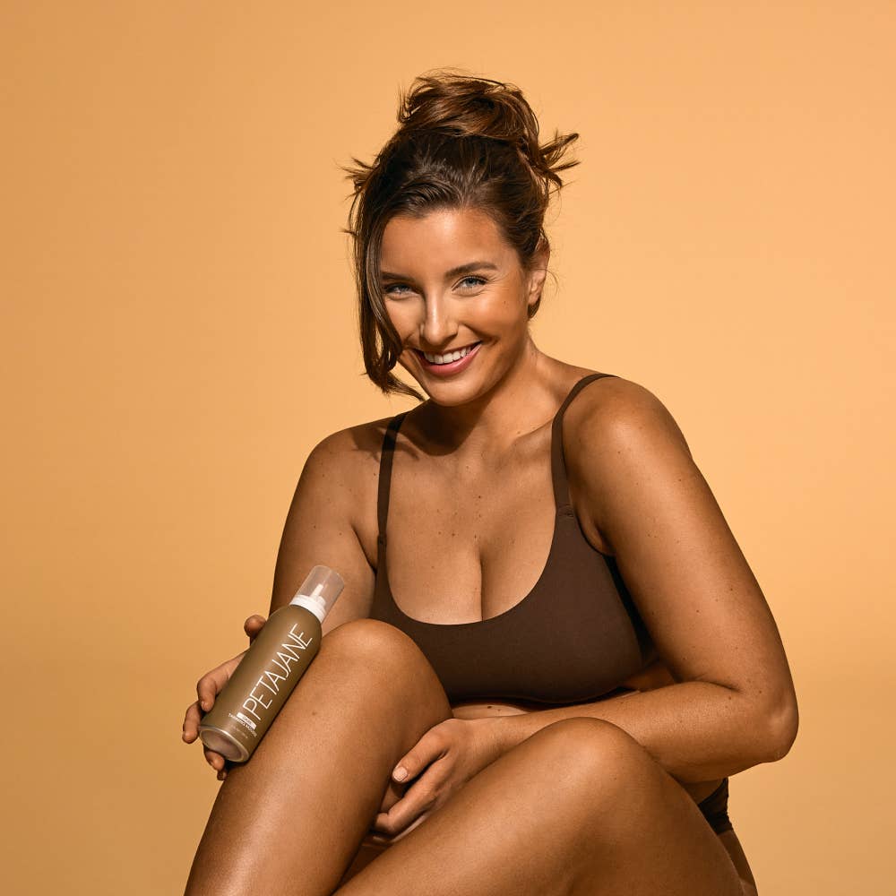 Woman holding a bottle of tanning mouse against a beige background