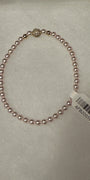 A single-strand pink pearl bracelet with a gold-toned decorative accent bead and a white product tag attached, displayed on a white textured surface.