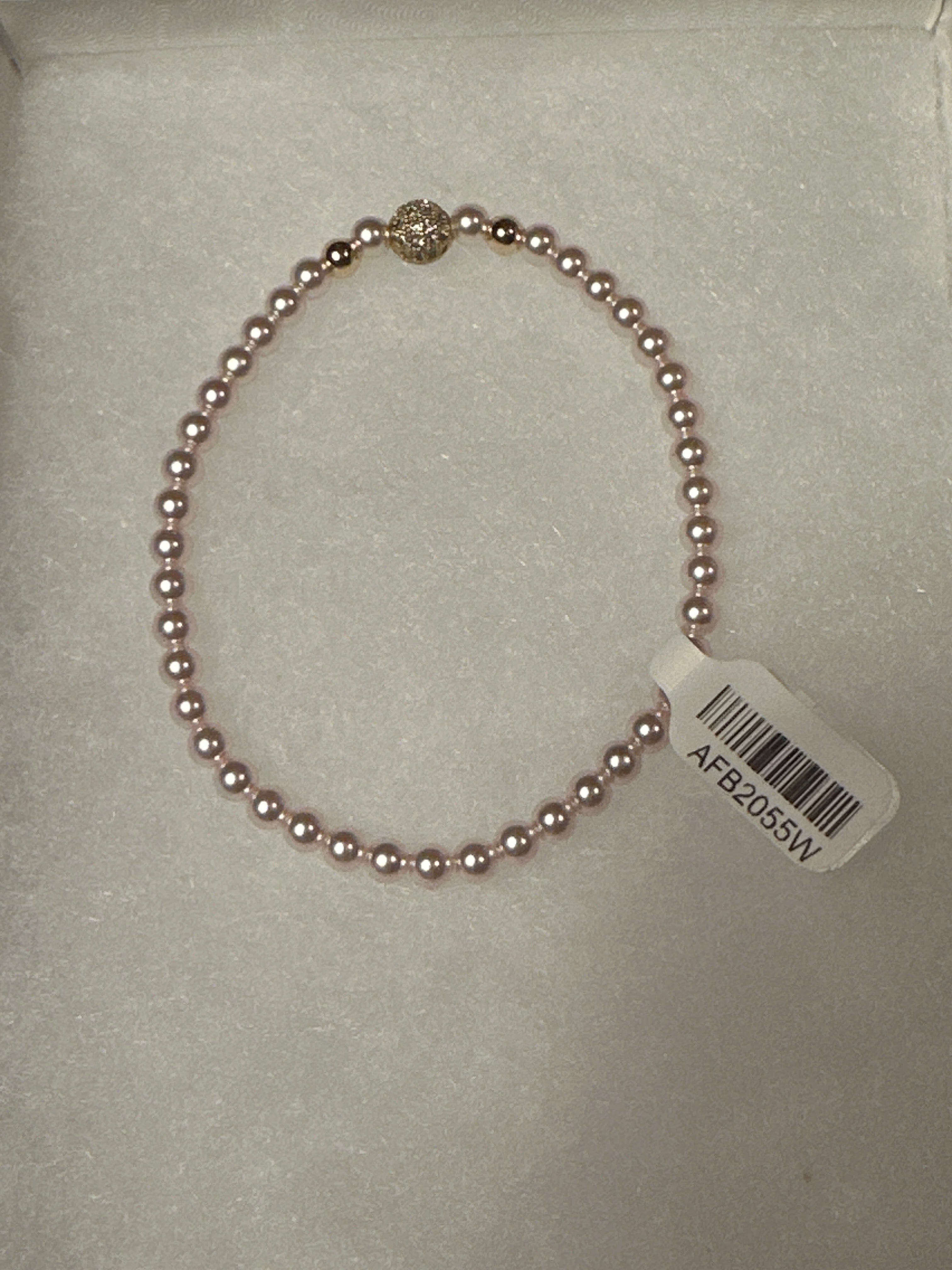 A single-strand pink pearl bracelet with a gold-toned decorative accent bead and a white product tag attached, displayed on a white textured surface.