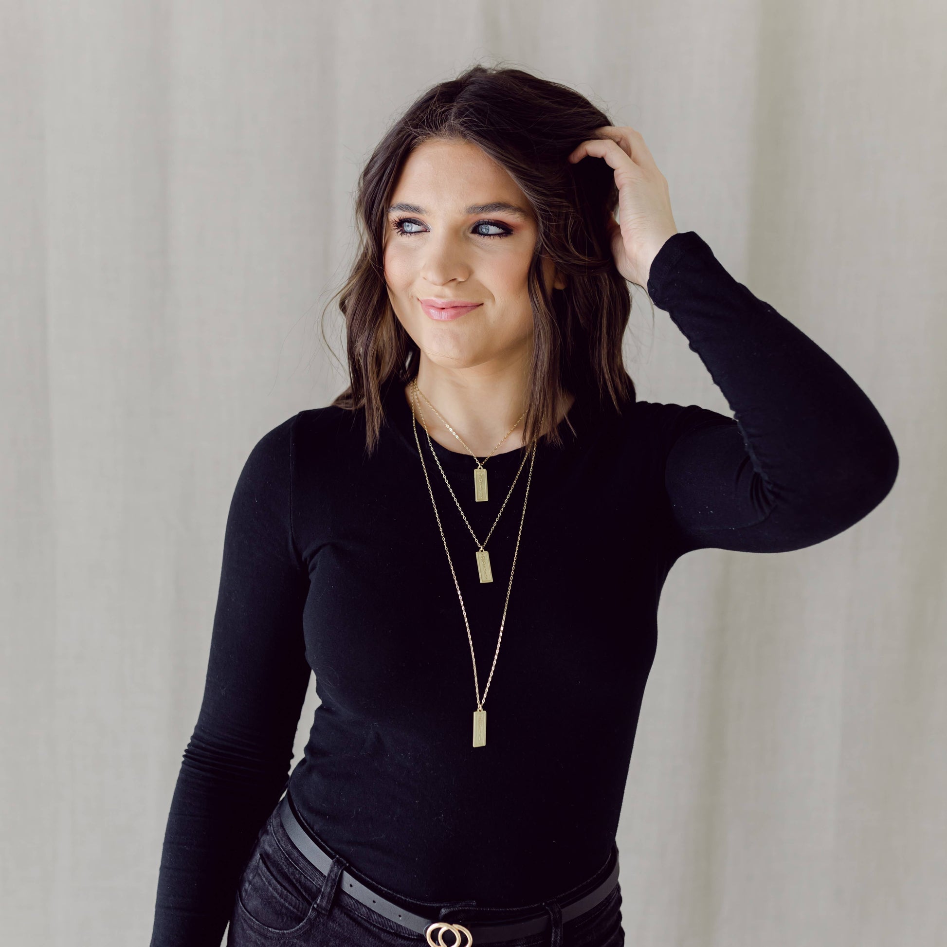 Woman wearing a black long-sleeve top and layered necklaces against a neutral background