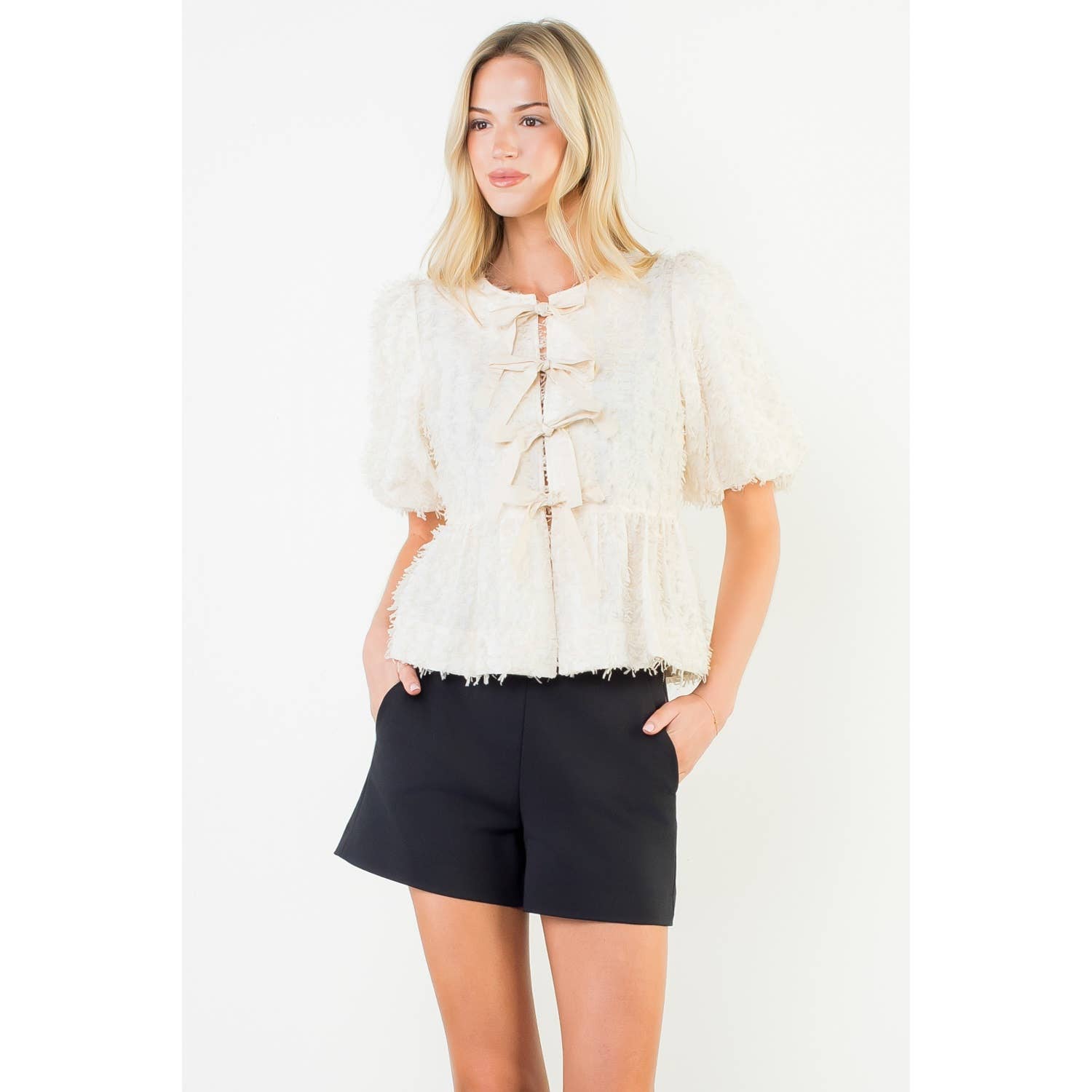 Woman wearing a white lace top and black shorts on a white background