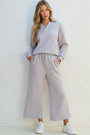 Woman wearing a light gray outfit with wide-leg pants against a white background