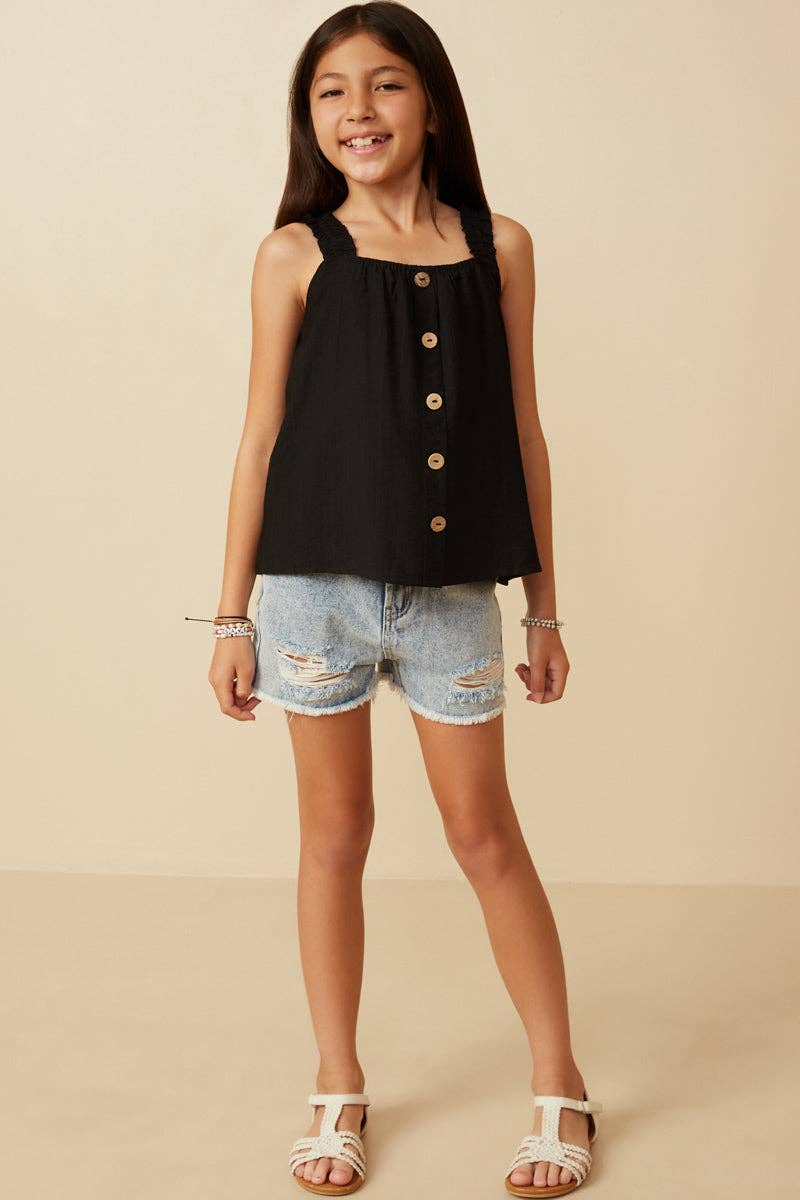 Young girl wearing a black sleeveless top with buttons and denim shorts on a beige background