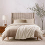 Neatly made bed with beige bedding and a white blanket in a bedroom setting.