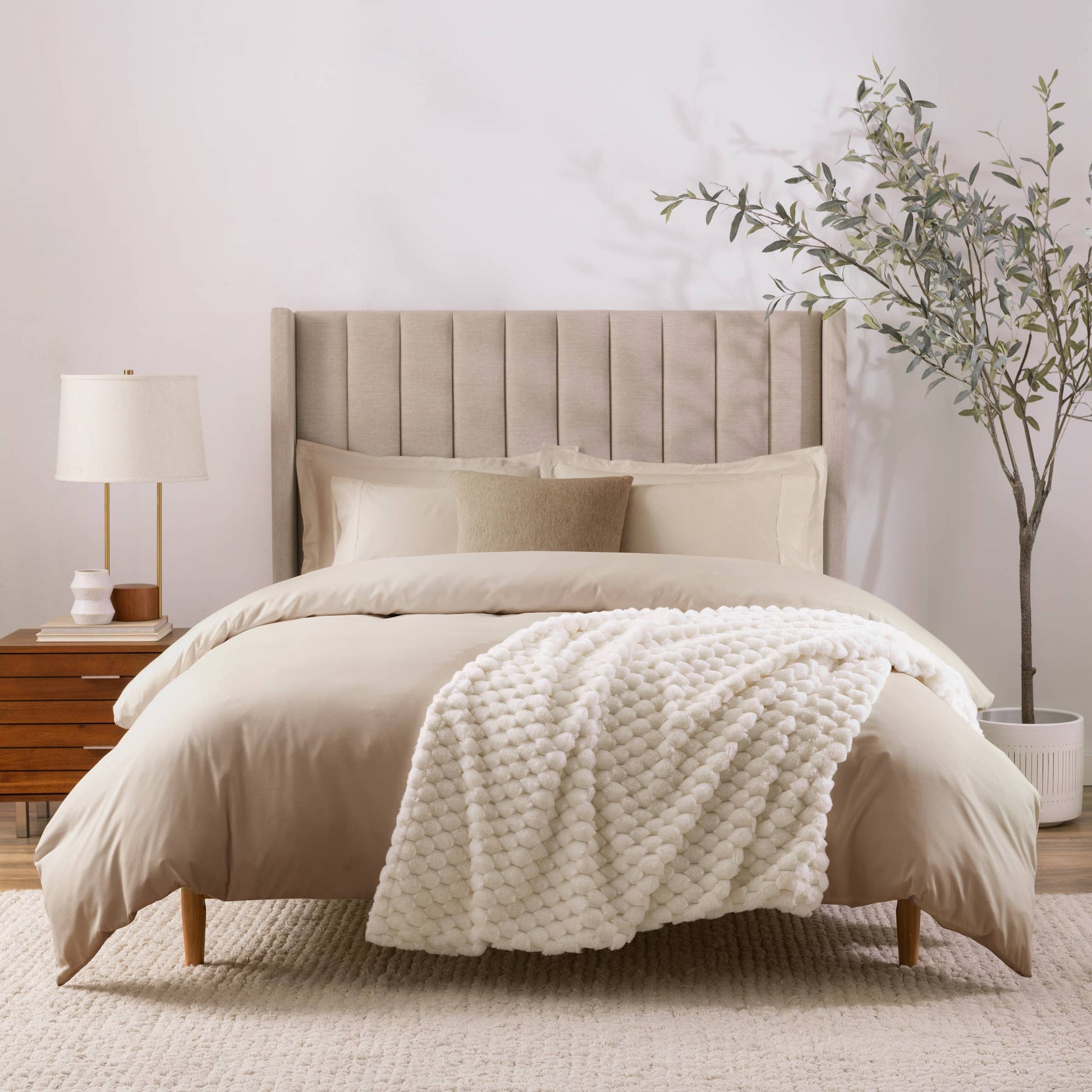 Neatly made bed with beige bedding and a white blanket in a bedroom setting.