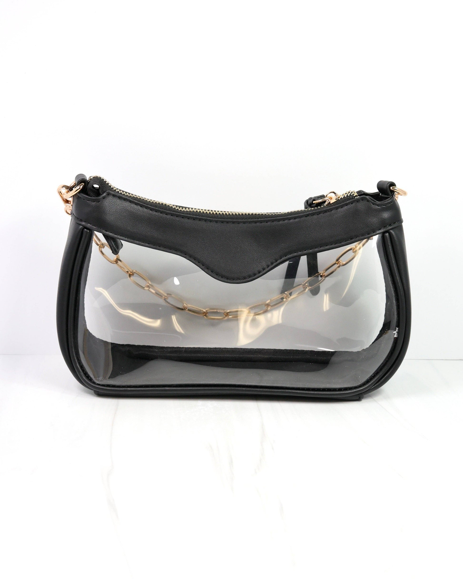 Black handbag with clear front section and gold chain strap on a white background