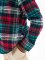 Close-up of a plaid shirt with a visible brand logo on a white background