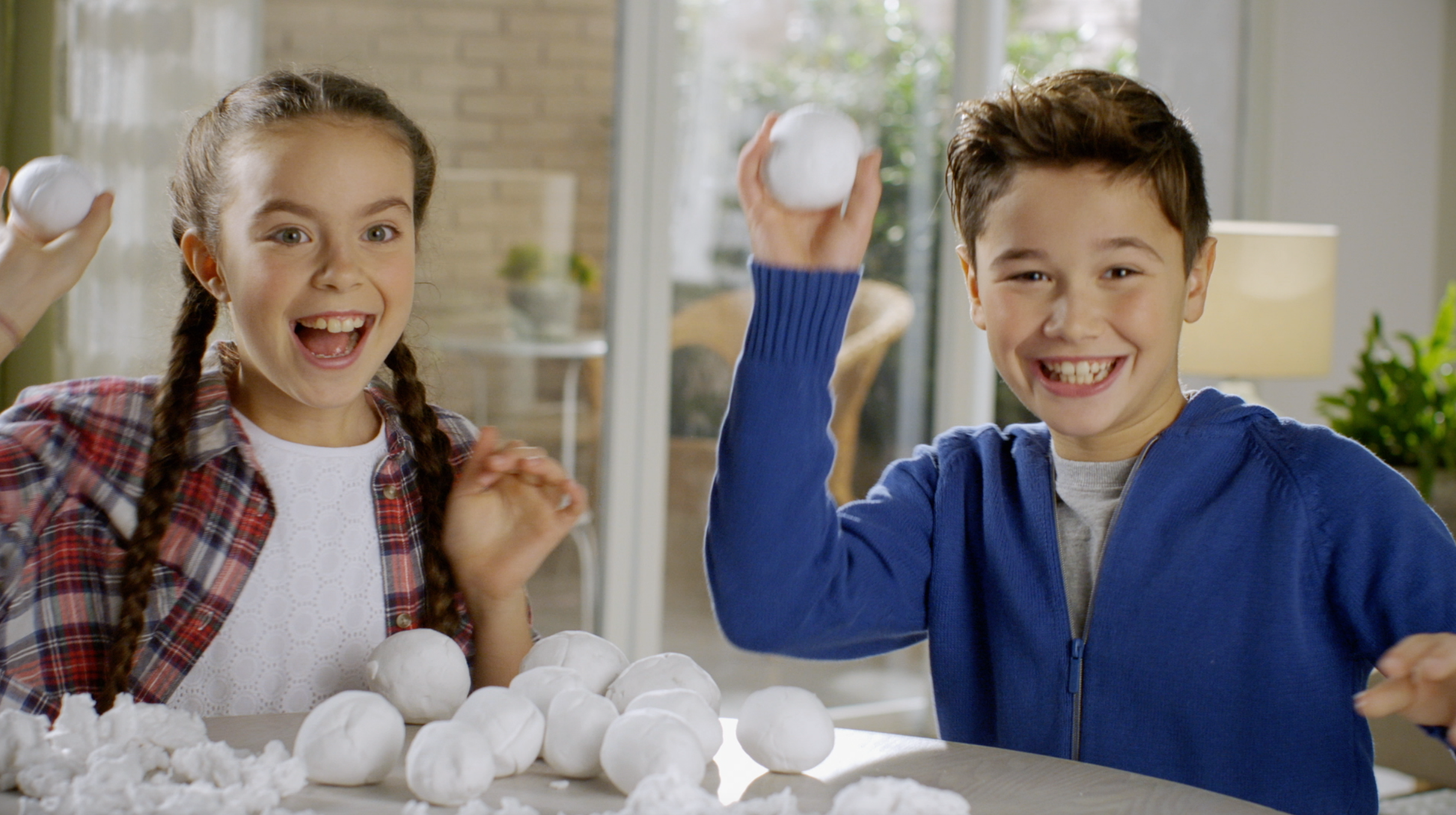 Two children playing with snowballs indoors, smiling and having fun.