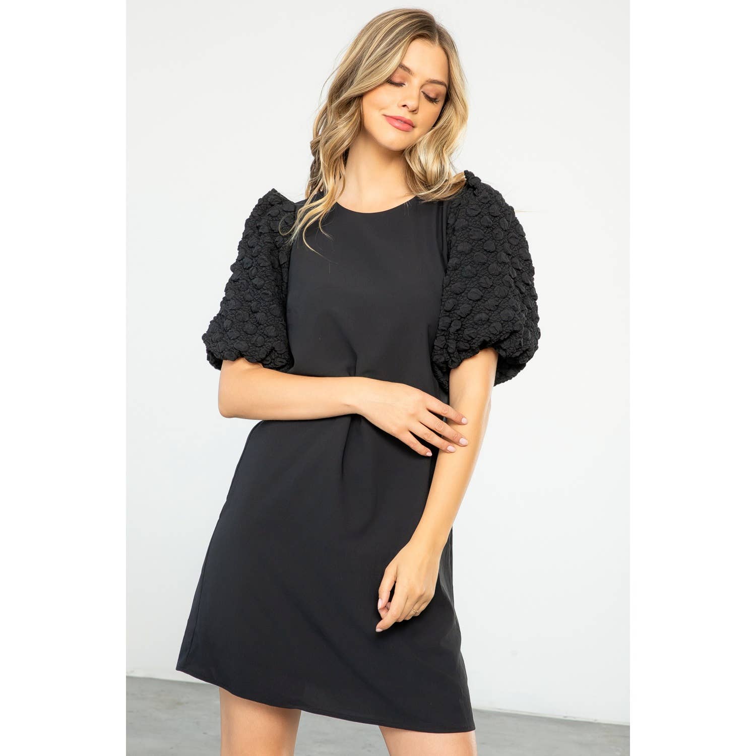 Woman wearing a black dress with a textured black shrug on a white background